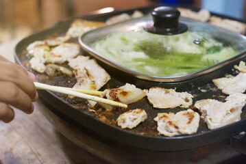 Wooden chopsticks tong barbecue pork on an Electric grilled aluminum pan  with soup barbecue party on a wooden table