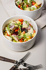 Close-up vegetarian salad with vegetables, mozzarella and fresh herbs in round white bowls on a light background. Organic delicious and healthy food. Vertical shot