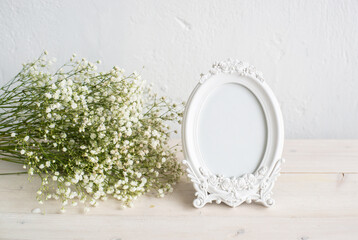 Portrait white picture frame mockup on wooden table. Modern ceramic vase with gypsophila. White wall background. Scandinavian interior.