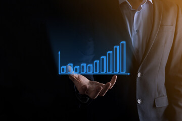 Business man holding holographic graphs and stock market statistics gain profits. Concept of growth planning and business strategy. Display of good economy form digital screen.