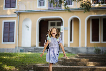 Fototapeta premium Happy little girl with school bag playing in front of school.