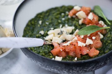 Risotto with spinach, tomato tartar and gorgonzola cheese served in a grey bowl, selective focus, closeup