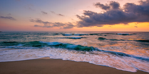 Fototapeta premium ocean beach with dramatic sky at sunrise. gorgeous vacation scenery. waves rolling on the sand in morning light