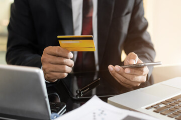 Male businessman use credit cards to conduct financial transactions through phones and laptop in...