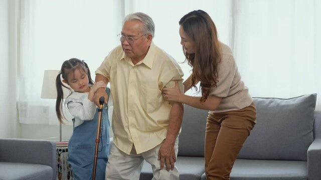 Asian family, Daughter and granddaughter take care support grandfather who is suffering from knee pain Got walking outside to take a walk And grandpa with a stick, elderly health care concept
