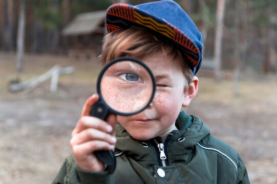 Happy child boy exploring nature with magnifying glass. Kid discovering world in part on spring and summer time. Forest school