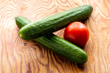 two cucumbers and a tomato on a wooden surface