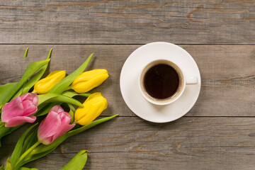 fresh pink tulips on gray wooden aged table top, good morning or greetings bouquet with white coffee cup