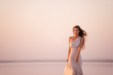 Fototapeta na wymiar Portrait of a young blonde woman in an evening airy pastel pink, powdery dress against a background of beautiful sunset. Girl with natural make-up, hair grows through the air. Copy space