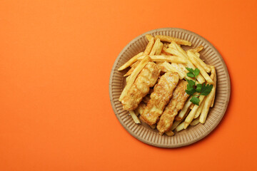 Plate with fried fish and chips on orange background