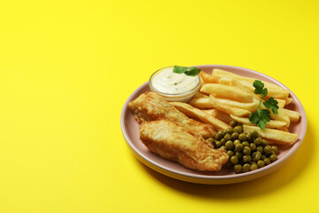Plate with fried fish and chips, pea and sauce on yellow background