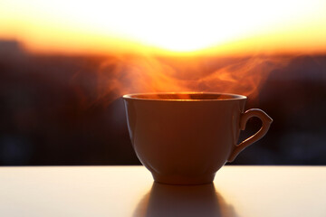 Hot coffee cup with smoke on sunrise background. Fresh start in the morning, cozy atmosphere