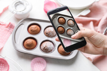 Female food photographer with mobile phone taking picture of tasty baked muffins, top view