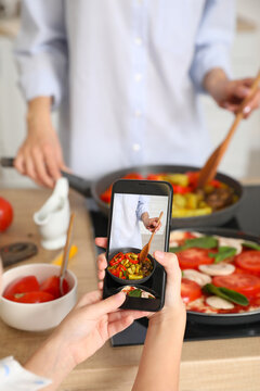 Little girl with mobile phone taking photo of female chef in kitchen