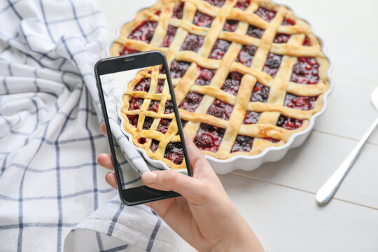 Female food photographer with mobile phone taking picture of tasty cranberry pie