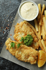 Baking paper with fried fish and chips on black smokey table