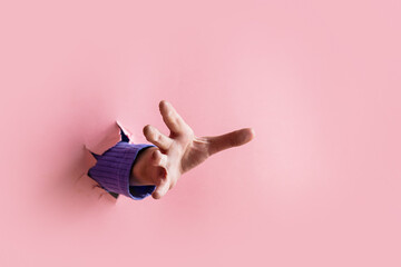 female hand trying to catch something sticking out from pink background - obrazy, fototapety, plakaty