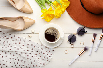 Cup of coffee with flowers, female clothes and accessories on white wooden background