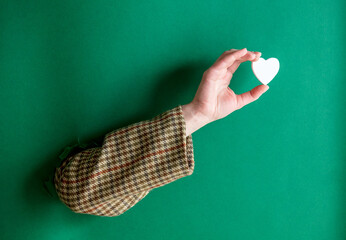 female hand hold little white heart on green background.