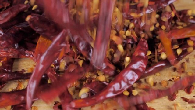 Exotic red pepper flakes and dried whole chilies dropping on a wooden table. Closeup shot of spicy hot red assorted chilies (lal mirchi) falling together 