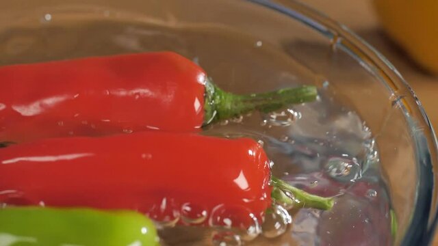 Rajasthani plump big red and green chilies in a bowl of water - spicy food . Closeup shot of hot and spicy mirchi with green stems in a transparent glass bowl on a wooden table