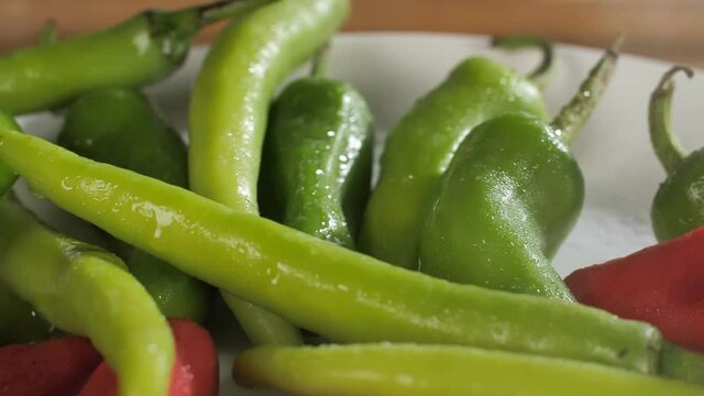Some fresh raw green and red chilies (hari and lal mirch) with a stream of water - Indian spice. Water droplets sprinkling on plump ripe pepper / Mirchi placed on a white background - spicy seasoning