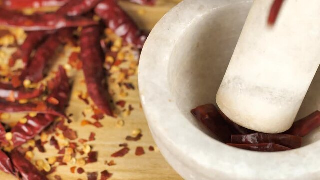 Air-dried roasted red chilies (lal mirch) falling inside a white marble mortar pestle. Closeup shot of whole hot red peppers for crushing - chili flakes / ingredient for seasoning
