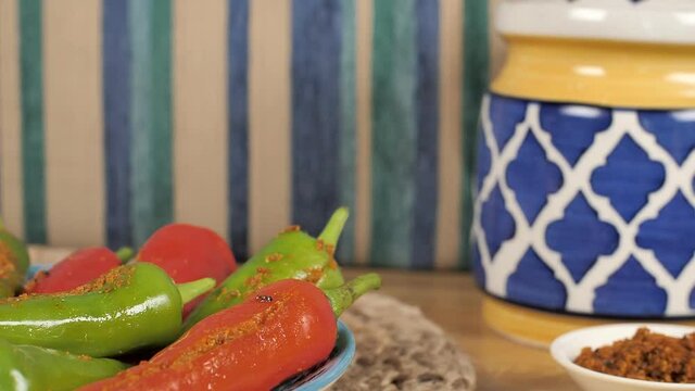 Stuffing Masala of Mirchi being placed on a wooden table - Indian Achaar. Closeup shot of red and green big chilies Indian pickle with a colorful jar placed against a colorful background
