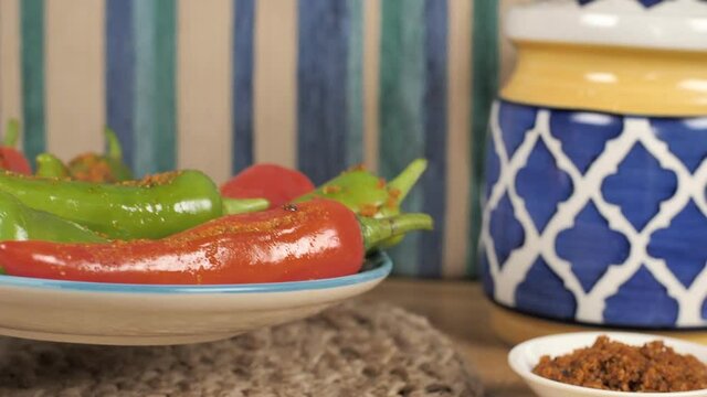 Female keeping a plate of red and green chilies pickle on the table. Closeup shot of Indian Mirchi Achaar stuffed with spicy flavorful Masala against a colorful background