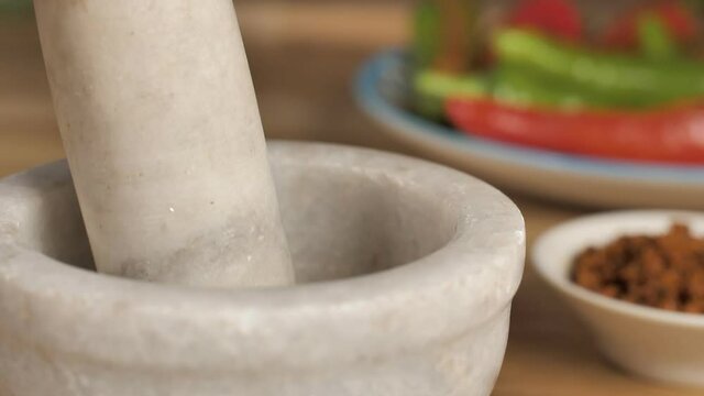 Traditional stone mortar pestle pounding ingredients to prepare spicy Masala. Grinding mortar pestle with red and green chilies and stuffing Masala for pickle in a blurred background