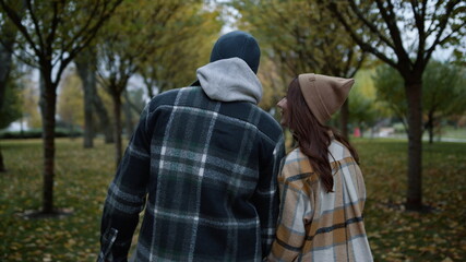 Back view of loving couple walking in autumn park in daytime. Close back view.