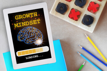 Growth mindset loading with brain on digital computer tablet with tic tac toe game and colored pencil on desk. Reskilling and up skilling concept and technology transformation learning model idea