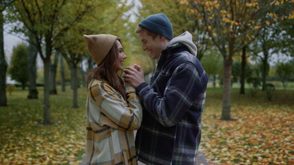 Smiling handsome boy warming girls hands by blowing steam in autumn weather. 