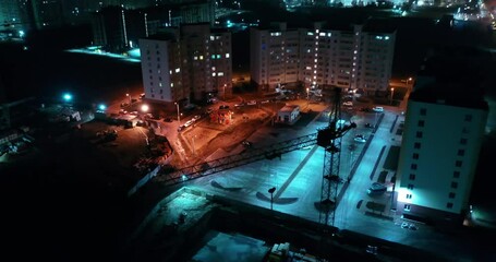 Night aerial shoot of flying above constructor crane in mysterious modern town. Unusual cool colors creating suspense atmosphere