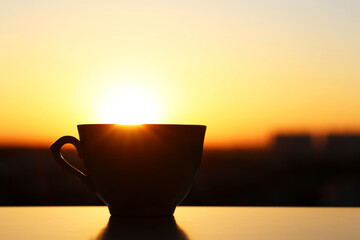 Silhouette of coffee cup on sunrise background, fresh start in the morning. Cozy atmosphere, city view from the window