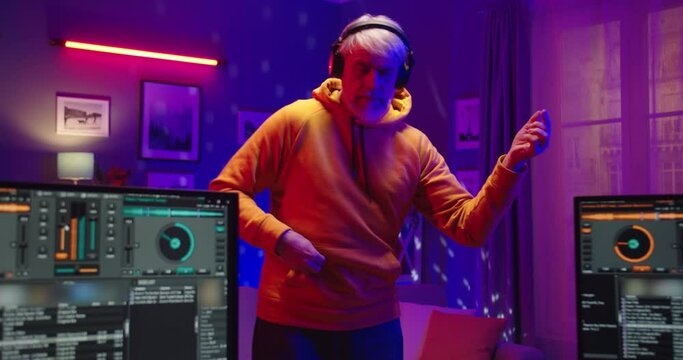 Portrait of funny joyful old Caucasian male musician in headphones pretending to play guitar standing at home recording studio in neon light. Man DJ listening to music creating new song, music concept