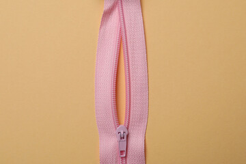 Pink zipper on beige background, close up