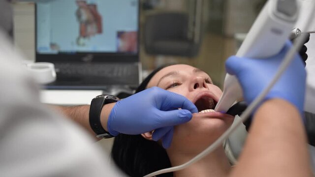 The doctor scans the patient's teeth in the clinic. The dentist is holding a hand-held 3D jaw and mouth scanner in his hand. Dental health. Creates a 3D model of teeth and gums on a medical monitor.