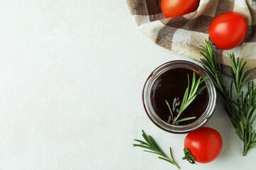 Jar of barbecue sauce, rosemary, tomatoes and kitchen towel on white textured table
