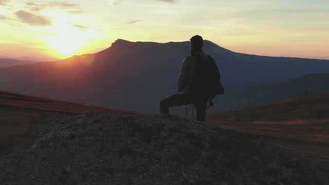 A tourist with a backpack watches a bright sunset in the mountains.
