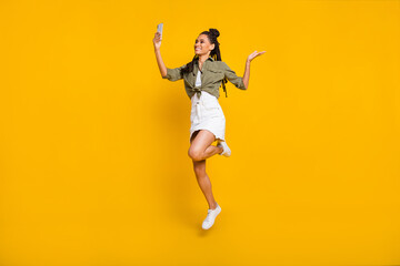 Fototapeta na wymiar Photo portrait full body view of dark skin girl jumping up taking selfie with phone isolated on vivid yellow colored background