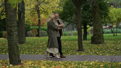 Side view shot of beautiful happy lovers walking along path among autumn trees. 