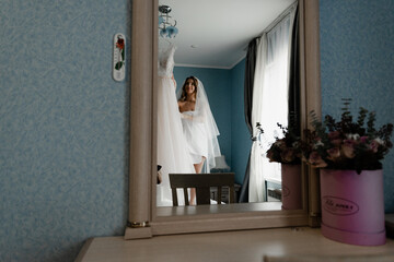 happy bride in a light robe holds her wedding dress in her hands. the bride gathers at home in her room. the girl is preparing for the wedding day.bride holding dress