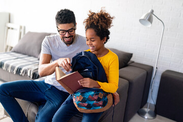 Black father helping daughter pack her bag for school