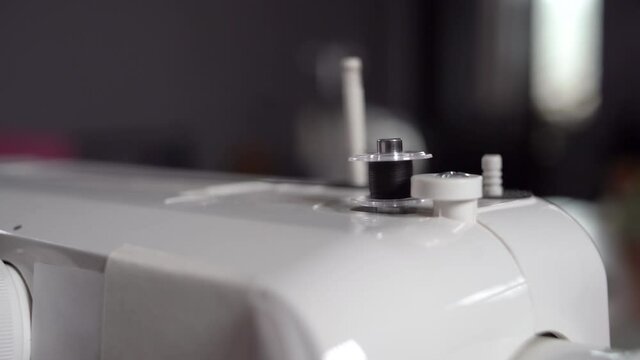 The designer winds the thread on the sewing machine. A small bobbin turns on the winder of a sewing machine and winds a white thread. Slow-motion auto-winding of white thread on sewing machine spool.