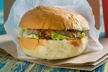 Burger with beef cutlet, sauce, salad and coffee to go in a paper cup side view, copy space close-up. Concept of food delivery, restaurant operation during quarantine covid 19