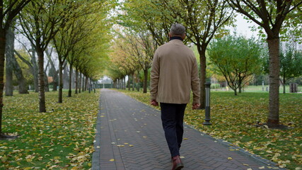 Fototapeta premium Casual man walking slowly through park in autumn weather. Mature senior going .