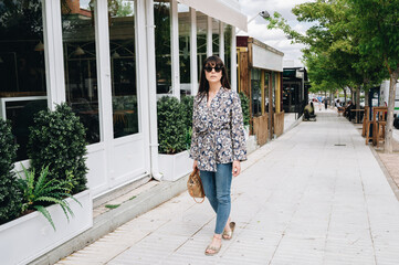 Obraz premium Lovely and chic woman walking along a shopping street on a sunny summer day.