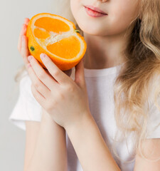 Smiling girl in a white t-shirt holding half an orange in her hands