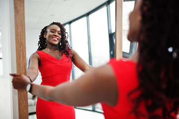 Magnificent young african woman in luxurious red dress in a luxury apartment look at mirror....